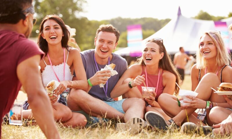 Friends sitting on grass and eating at music festival